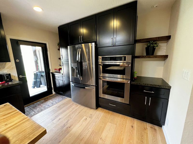 Modern kitchen featuring stainless steel refrigerator and oven, black cabinetry, wooden countertop, and door leading outside, reflecting quality craftsmanship in home restoration.